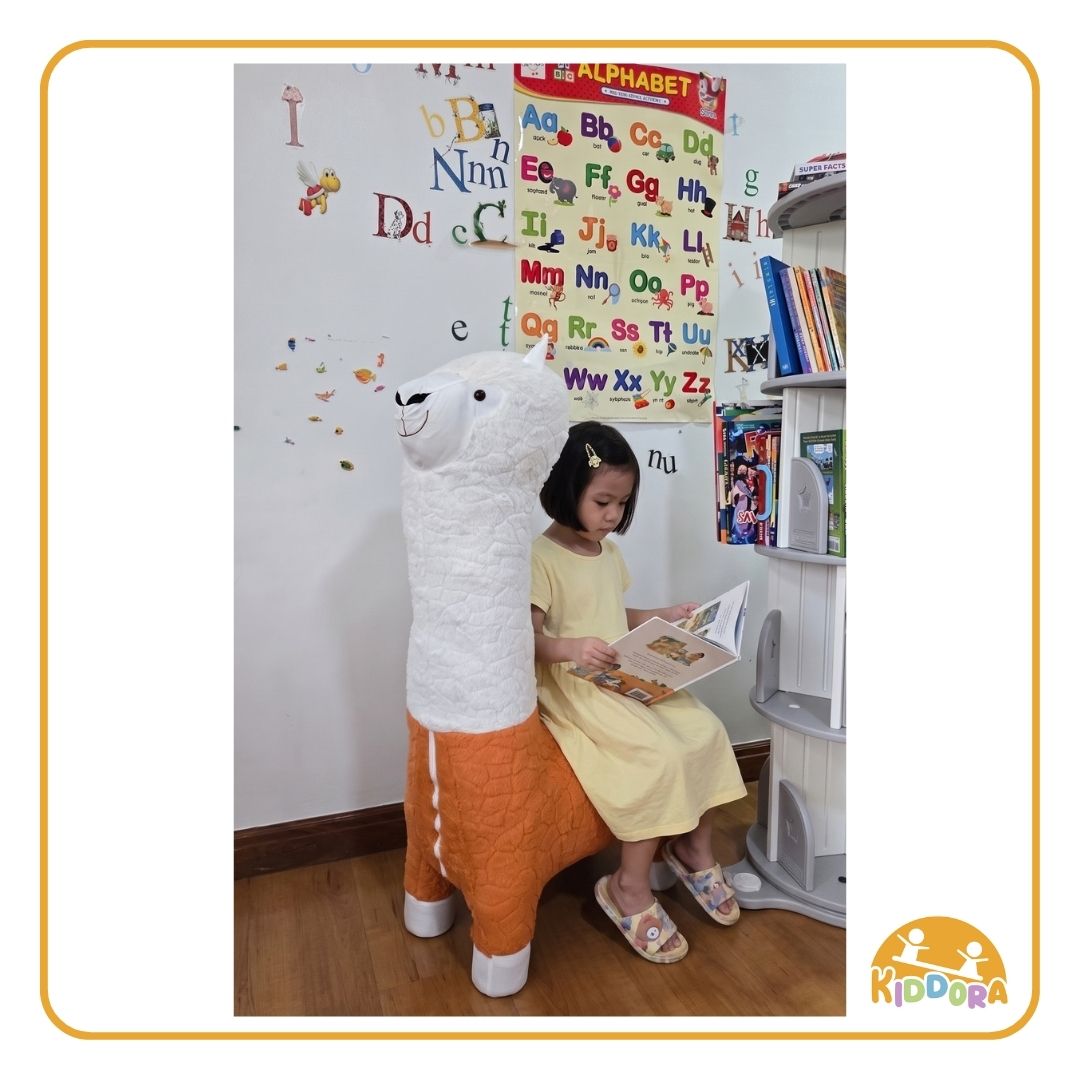 Child reading a book while sitting on the orange Alpaca Plush Kids Stool